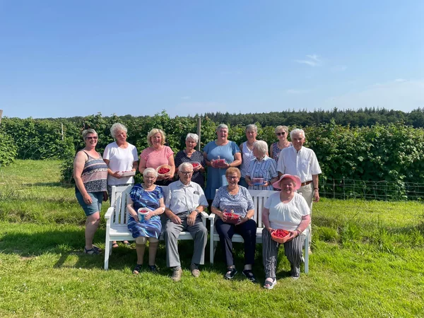 Besucher*innen sitzend und stehend vor dem Himbeerfeld mit frisch gepflückten Himbeeren